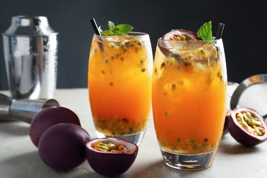 Photo of Tasty passion fruit drink with mint in glasses and fresh fruits on gray table, closeup