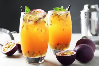 Photo of Tasty passion fruit drink with mint in glasses and fresh fruits on gray table, closeup