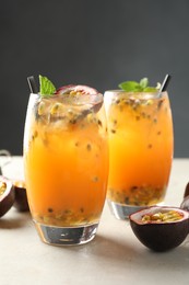 Photo of Tasty passion fruit drink with mint in glasses and fresh fruits on gray table, closeup