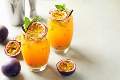 Photo of Tasty passion fruit drink with mint in glasses and fresh fruits on gray table, closeup. Space for text