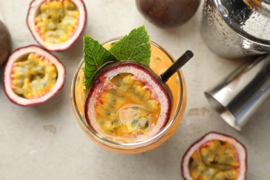Photo of Tasty passion fruit drink with mint in glass, fresh fruits, shaker and jigger on gray table, flat lay