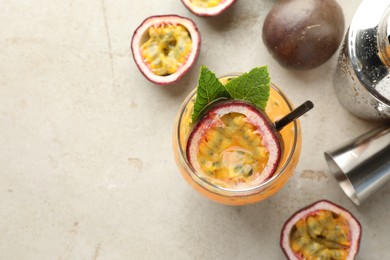 Photo of Tasty passion fruit drink with mint in glass, fresh fruits, shaker and jigger on gray table, flat lay. Space for text
