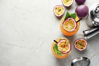 Photo of Tasty passion fruit drink with mint in glasses, fresh fruits and bartender's tools on gray textured table, flat lay. Space for text