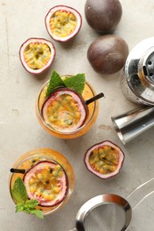 Photo of Tasty passion fruit drink with mint in glasses, fresh fruits and bartender's tools on gray textured table, flat lay