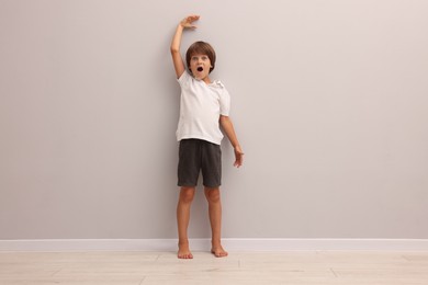 Photo of Little boy measuring his height near light grey wall indoors