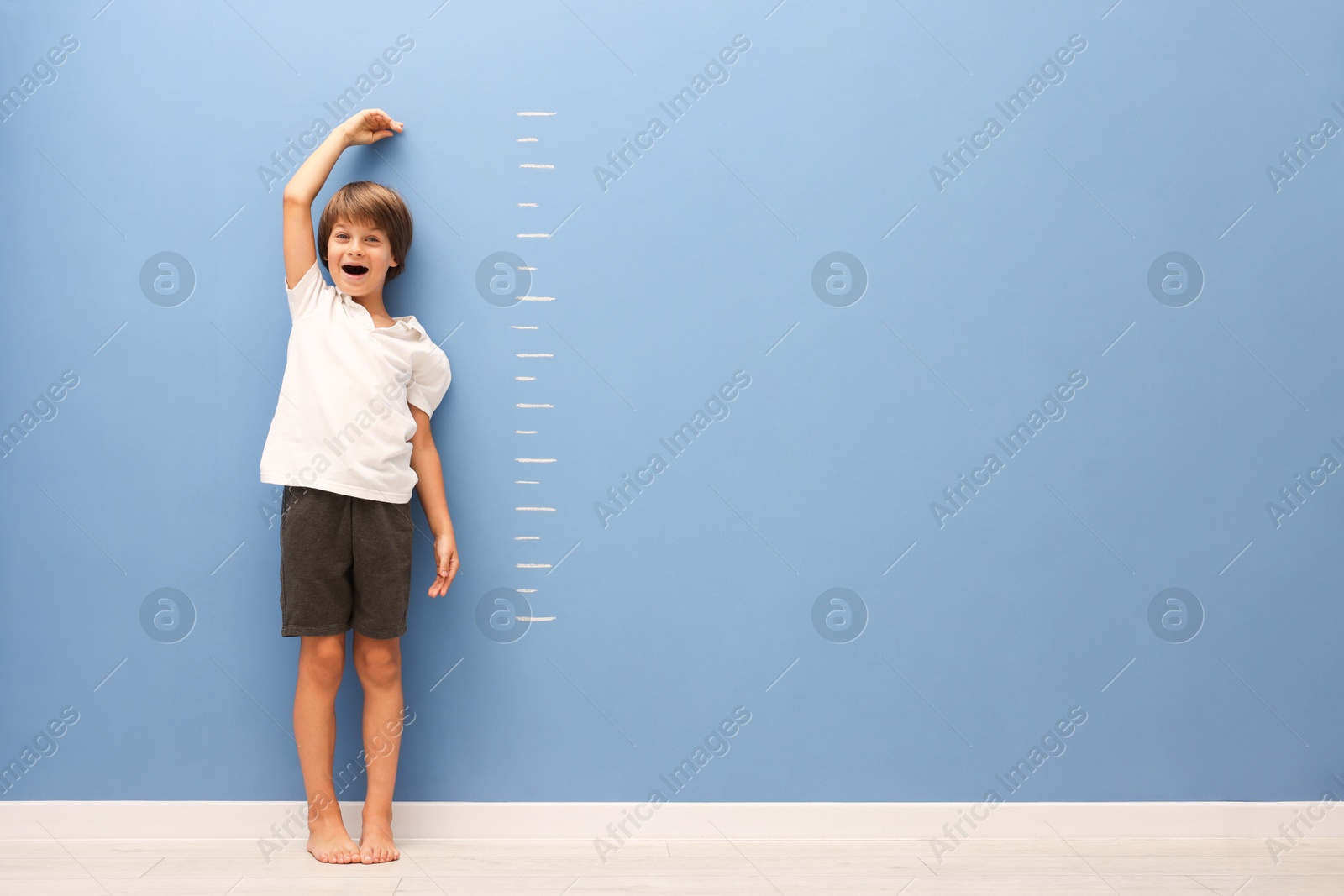 Photo of Little boy measuring his height near blue wall indoors. Space for text