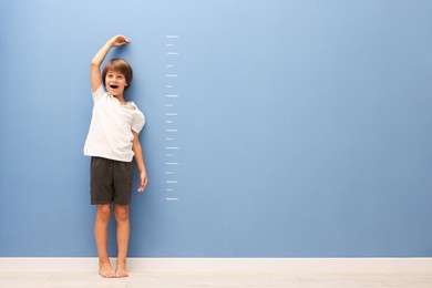 Photo of Little boy measuring his height near blue wall indoors. Space for text