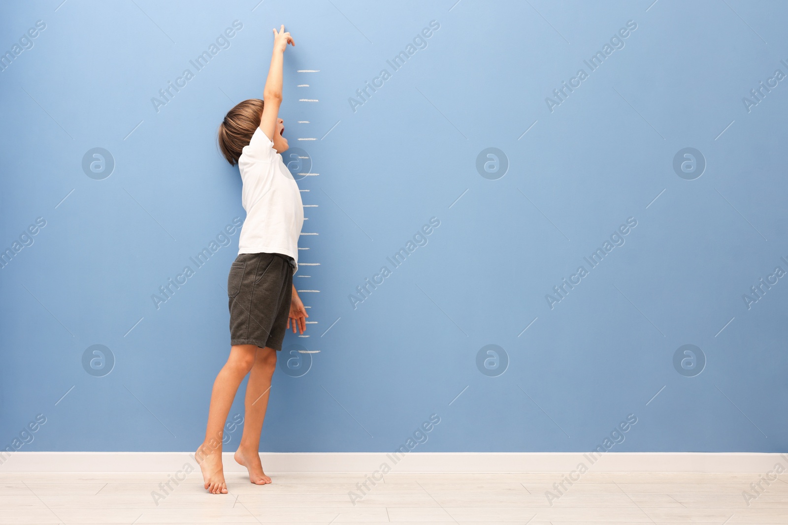 Photo of Little boy measuring his height near blue wall indoors. Space for text