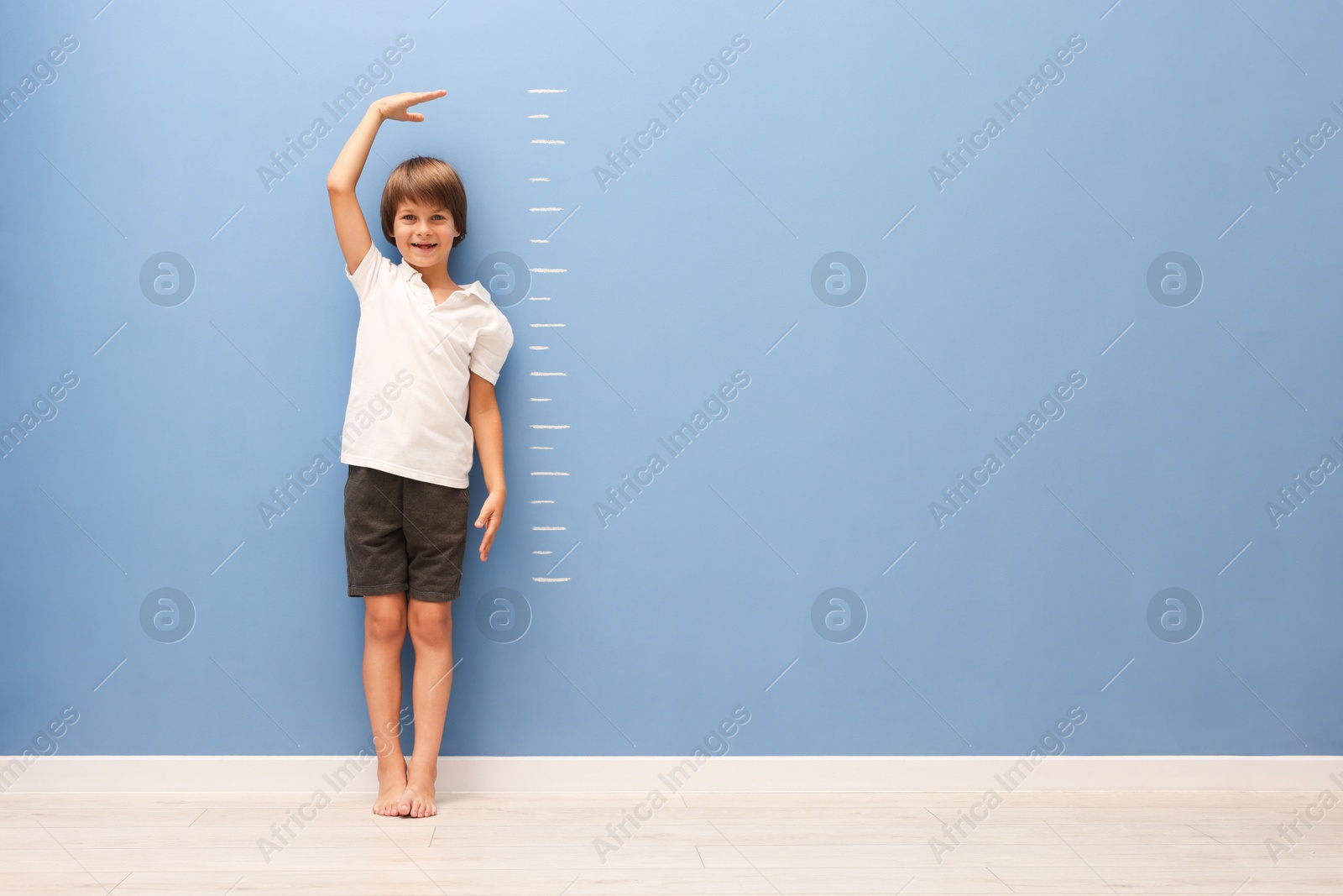 Photo of Little boy measuring his height near blue wall indoors. Space for text