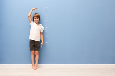 Photo of Little boy measuring his height near blue wall indoors. Space for text