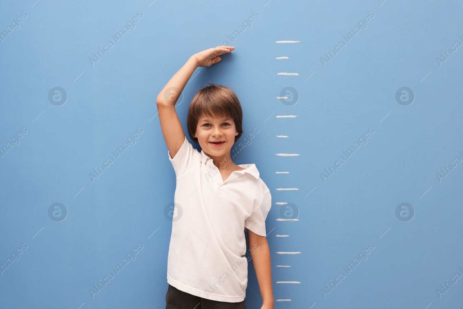 Photo of Little boy measuring his height near blue wall indoors