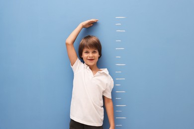 Photo of Little boy measuring his height near blue wall indoors