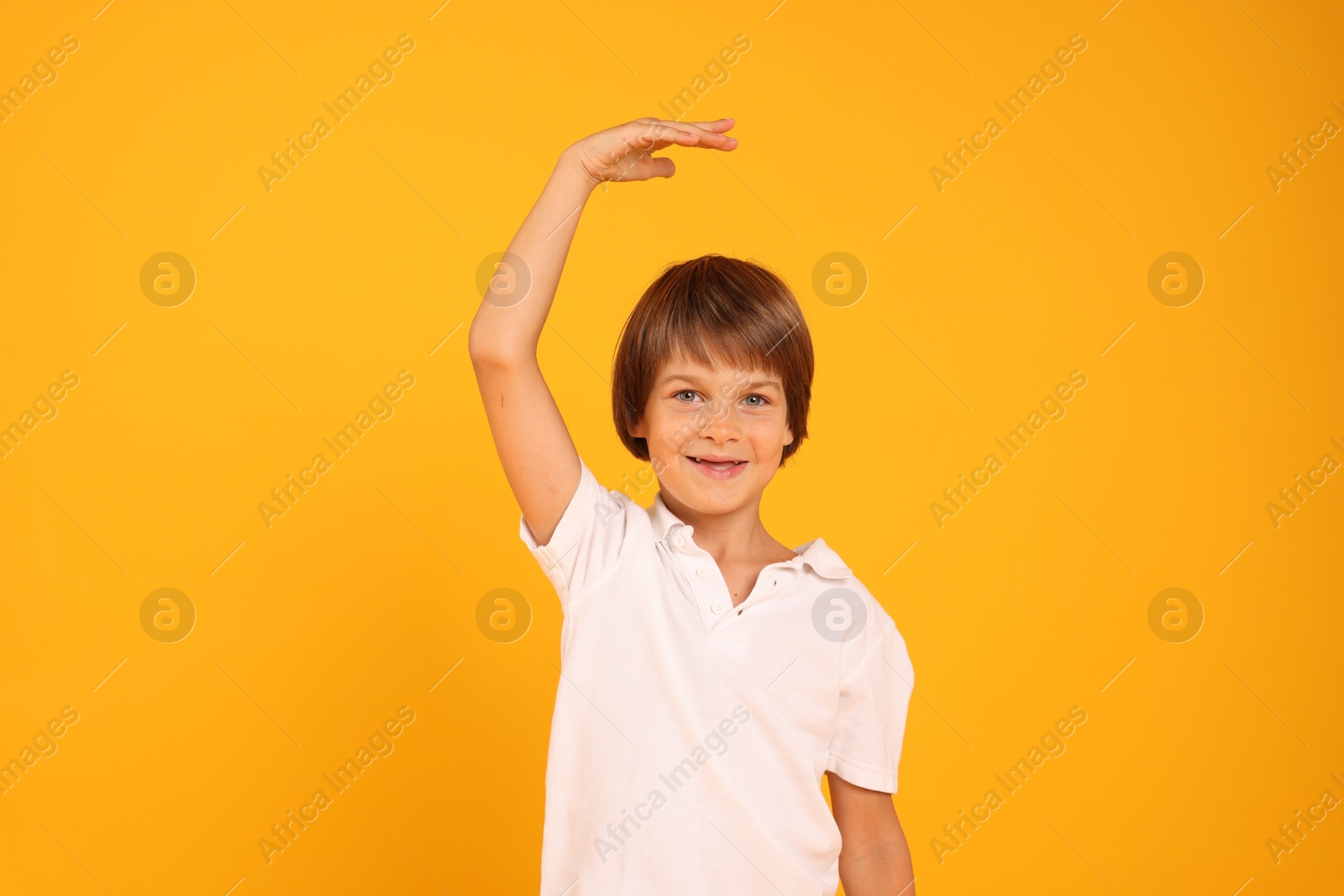 Photo of Little boy measuring his height on orange background