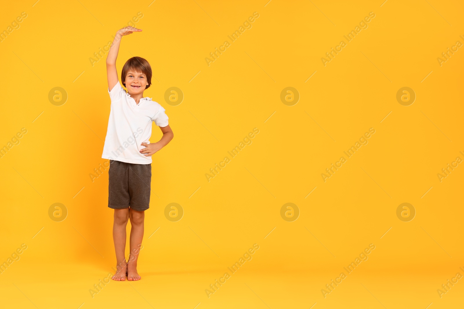 Photo of Little boy measuring his height on orange background, space for text