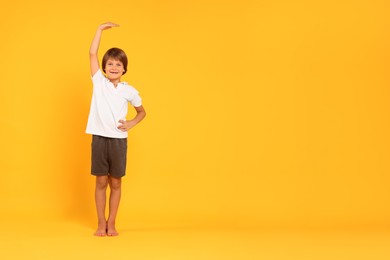 Photo of Little boy measuring his height on orange background, space for text
