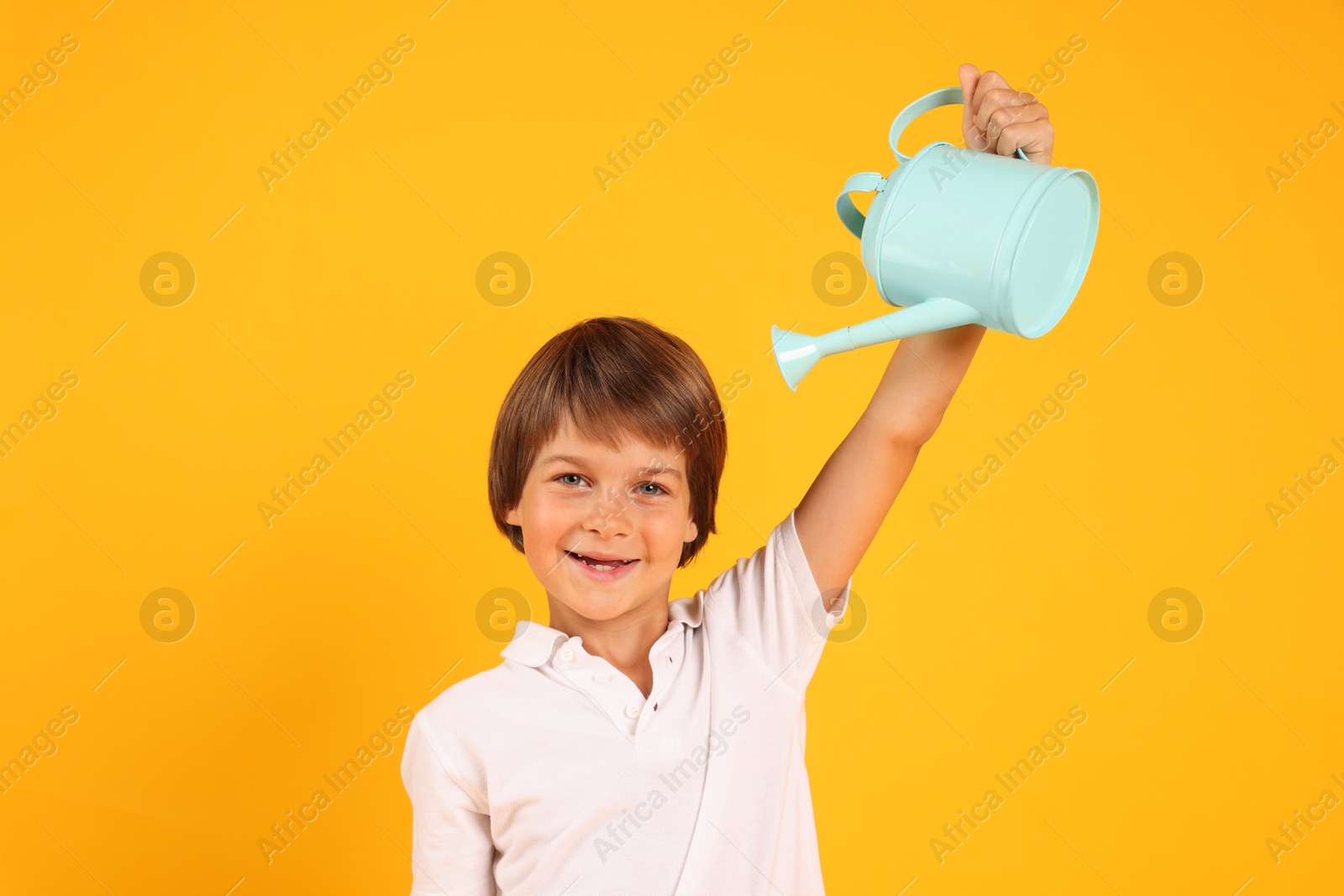 Photo of Little boy with watering can on orange background. Grow up faster