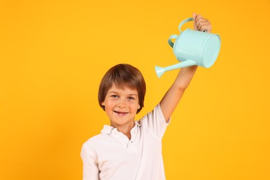 Photo of Little boy with watering can on orange background. Grow up faster