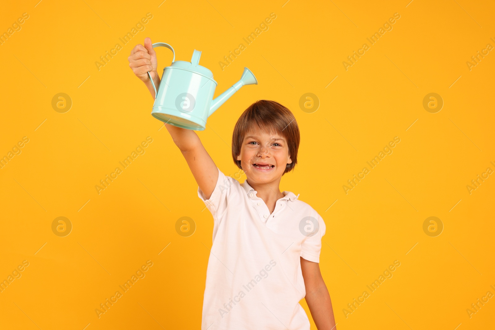Photo of Little boy with watering can on orange background. Grow up faster