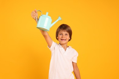 Photo of Little boy with watering can on orange background. Grow up faster