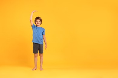 Photo of Little boy measuring his height on orange background, space for text