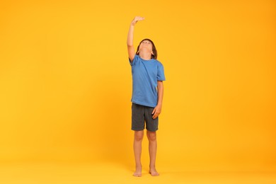 Photo of Little boy measuring his height on orange background
