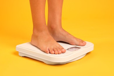 Photo of Little boy standing on scales against orange background, closeup