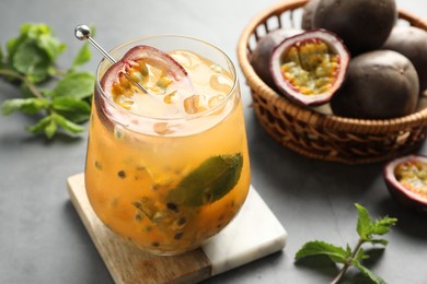 Photo of Tasty passion fruit drink in glass, fresh fruits and mint on gray table, closeup