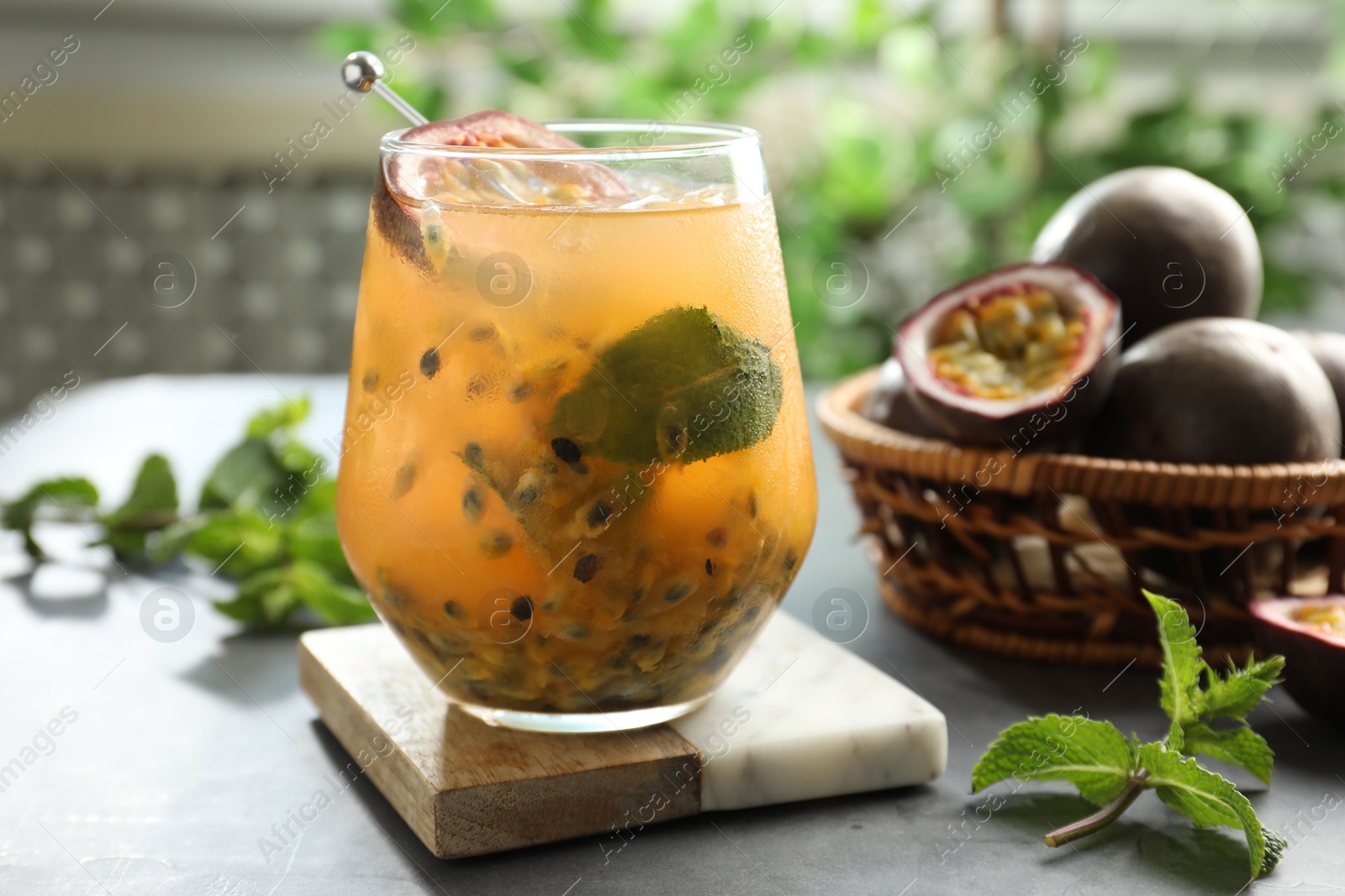 Photo of Tasty passion fruit drink in glass, fresh fruits and mint on gray table, closeup