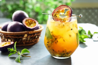 Photo of Tasty passion fruit drink in glass, fresh fruits and mint on gray table, closeup