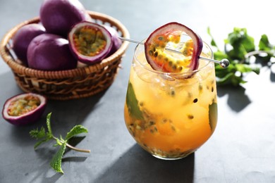 Photo of Tasty passion fruit drink in glass, fresh fruits and mint on gray table, closeup