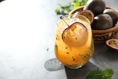 Photo of Tasty passion fruit drink in glass, fresh fruits and mint on gray table, closeup. Space for text