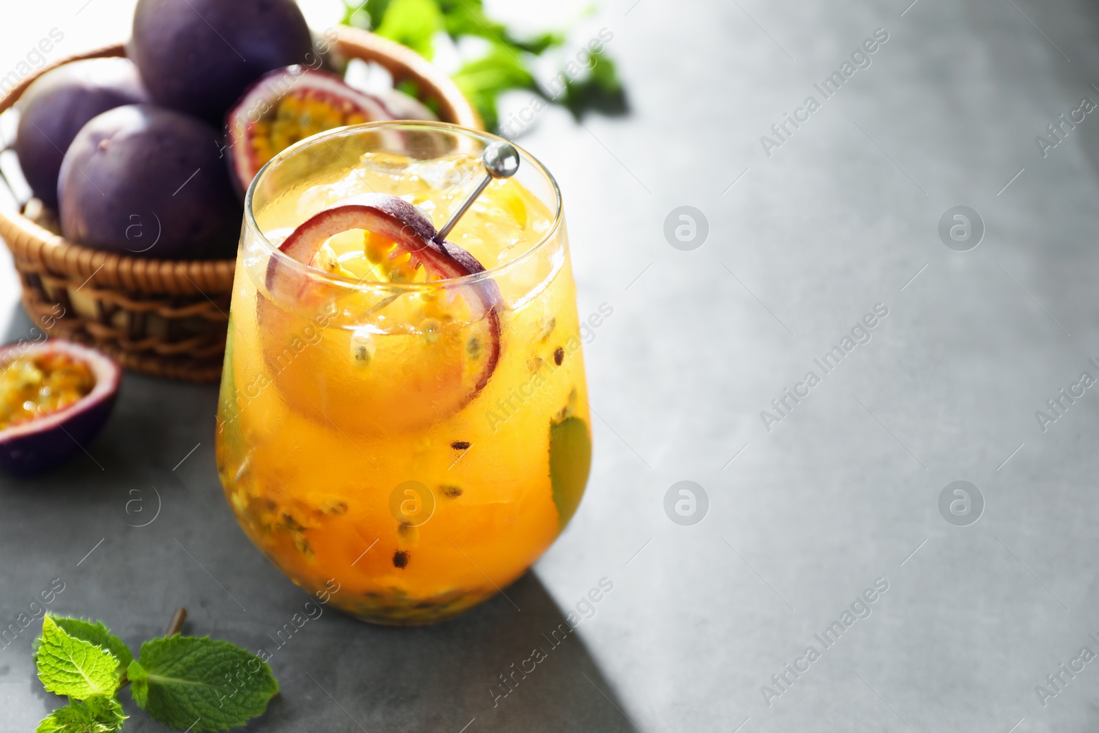 Photo of Tasty passion fruit drink in glass, fresh fruits and mint on gray table, closeup. Space for text