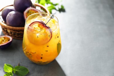 Photo of Tasty passion fruit drink in glass, fresh fruits and mint on gray table, closeup. Space for text