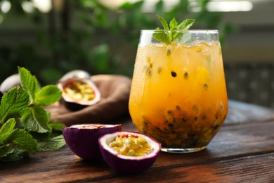 Photo of Tasty passion fruit drink with mint in glass and fresh fruits on wooden table, closeup