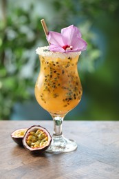 Photo of Tasty passion fruit drink in glass decorated with hibiscus flower on wooden table against blurred green background