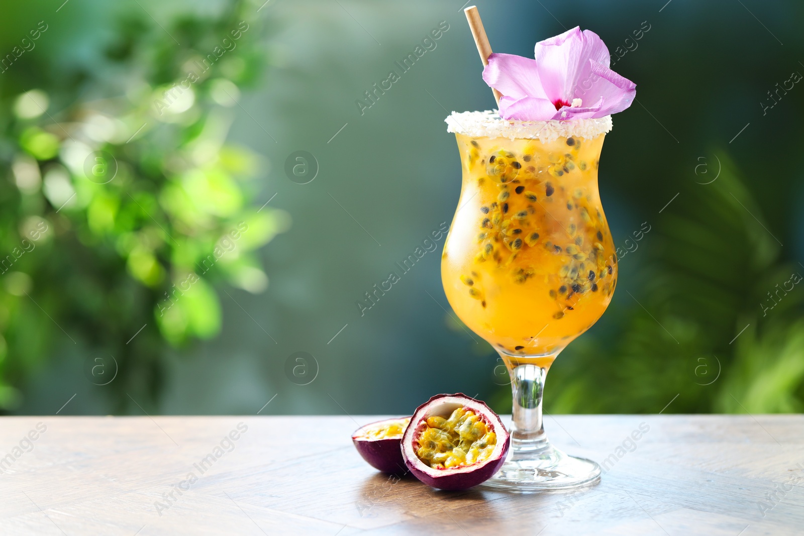Tasty passion fruit drink in glass decorated with hibiscus flower on wooden table against blurred green background. Space for text Photo of Tasty passion fruit drink in glass decorated with hibiscus flower on wooden table against blurred green background. Space for text