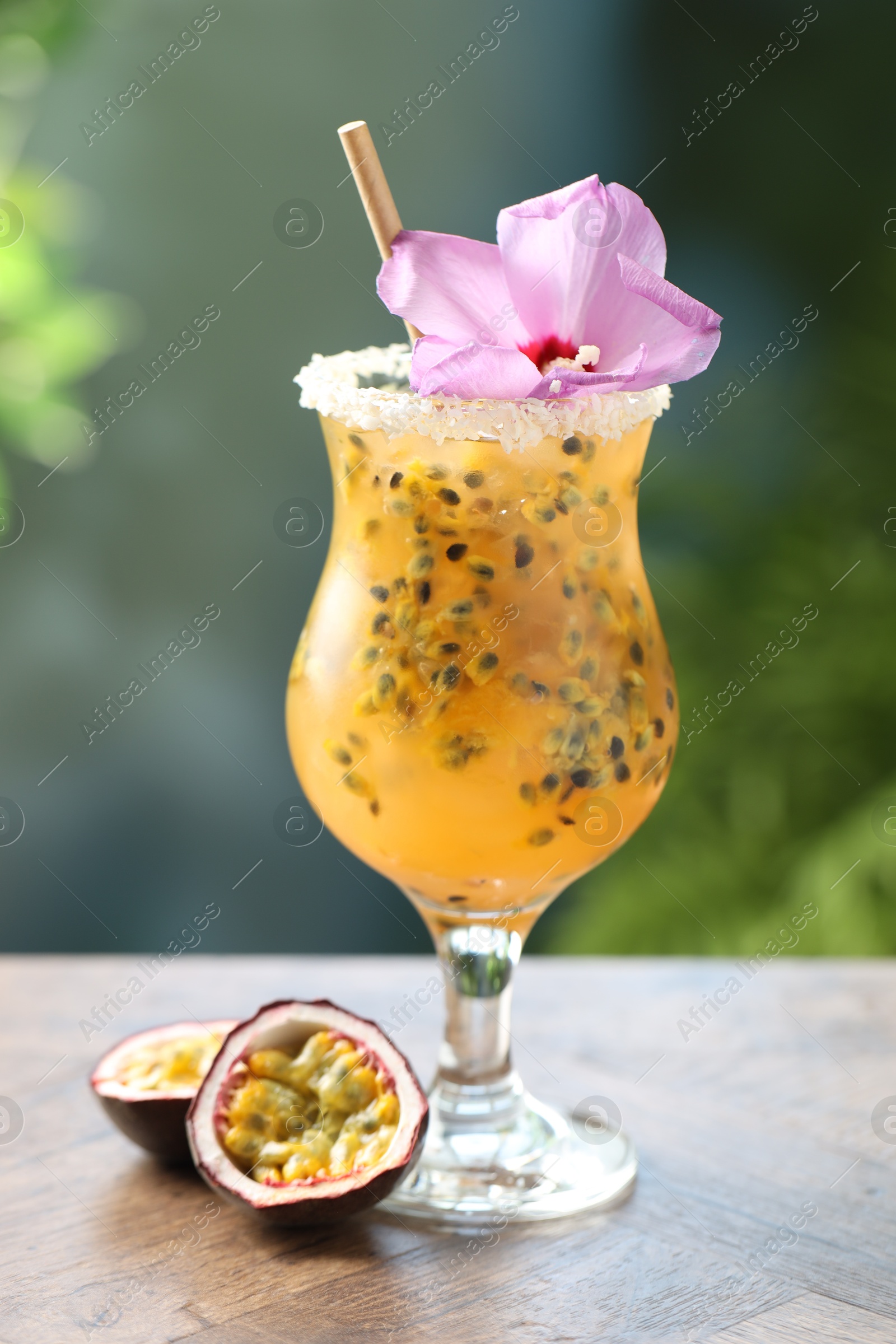 Tasty passion fruit drink in glass decorated with hibiscus flower on wooden table against blurred green background Photo of Tasty passion fruit drink in glass decorated with hibiscus flower on wooden table against blurred green background