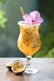 Photo of Tasty passion fruit drink in glass decorated with hibiscus flower on wooden table against blurred green background