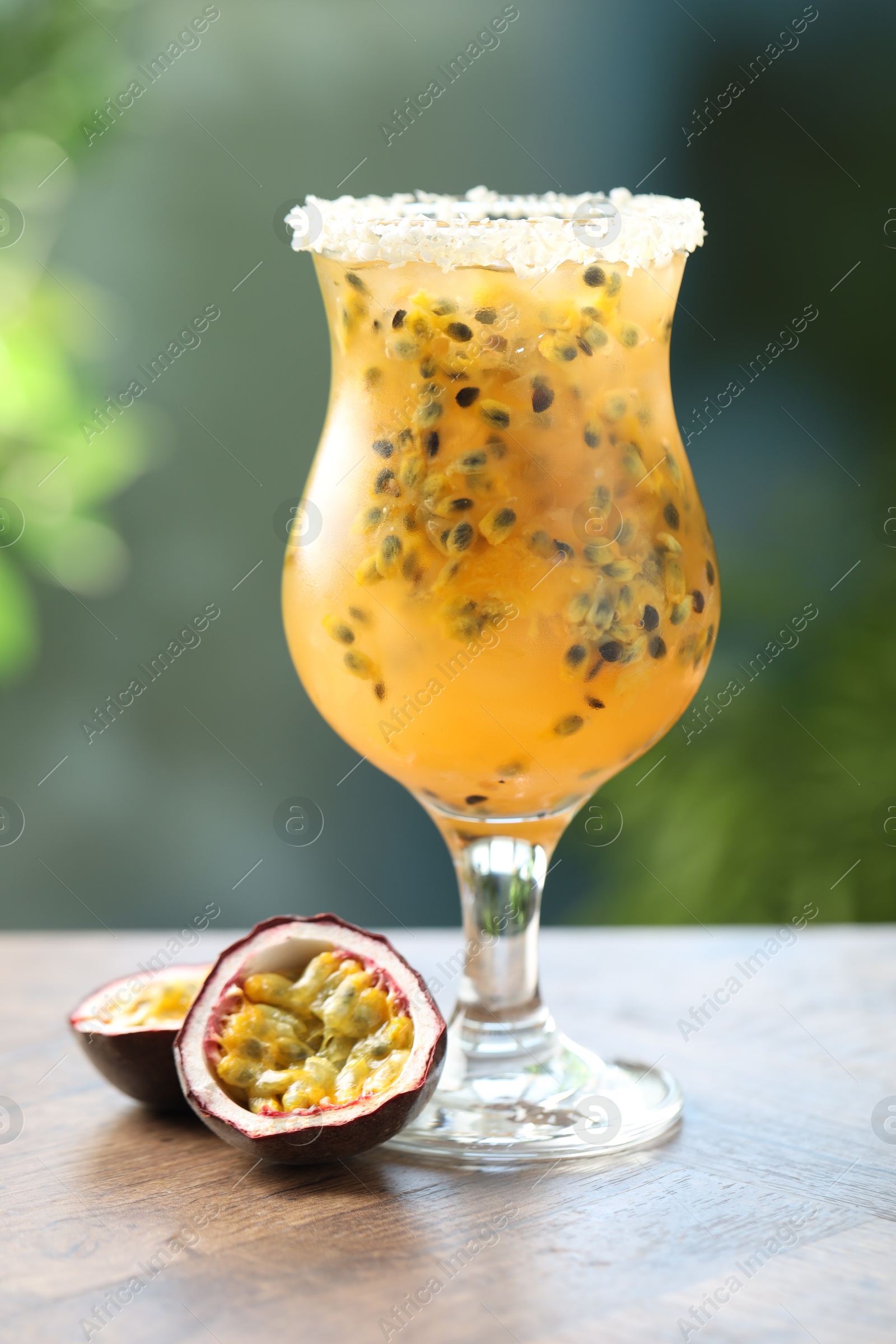 Photo of Tasty passion fruit drink in glass and fresh fruits on wooden table against blurred green background