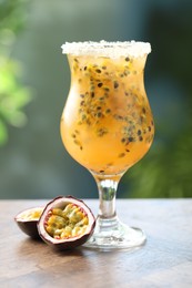Photo of Tasty passion fruit drink in glass and fresh fruits on wooden table against blurred green background
