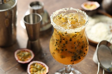 Photo of Tasty passion fruit drink in glass, fresh fruits and bartender's tools on table, closeup