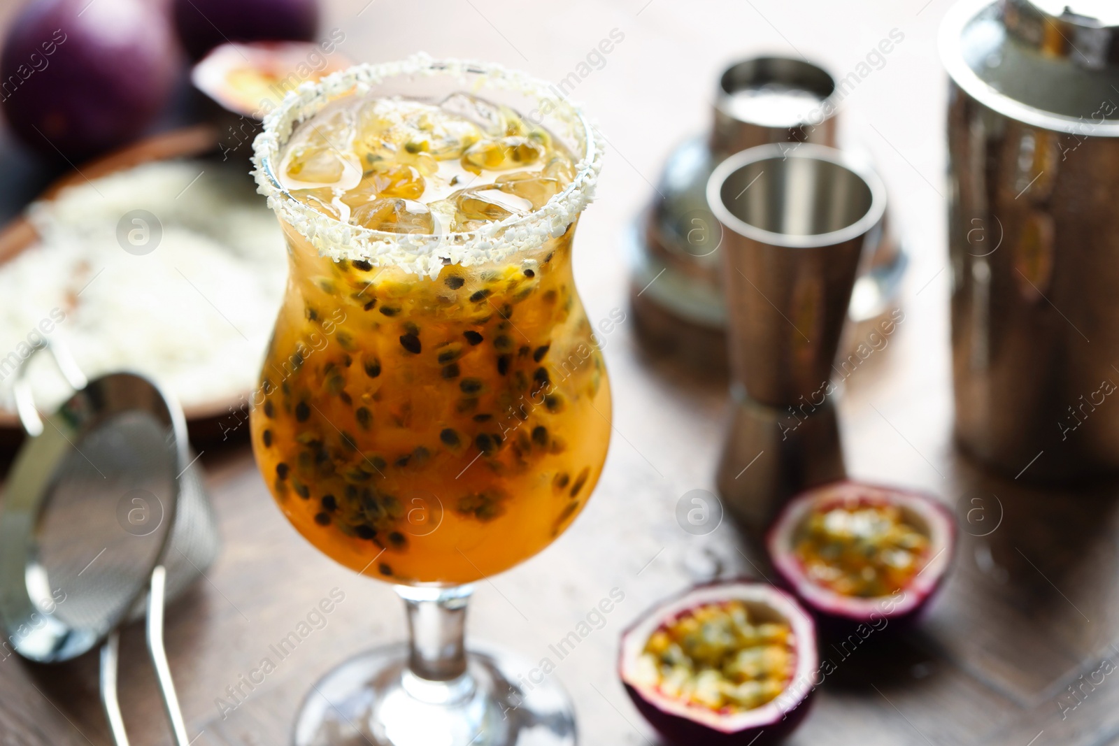 Photo of Tasty passion fruit drink in glass, fresh fruits and bartender's tools on table, closeup