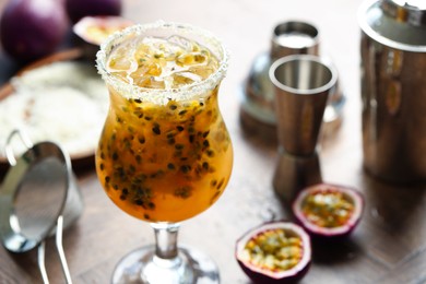 Photo of Tasty passion fruit drink in glass, fresh fruits and bartender's tools on table, closeup