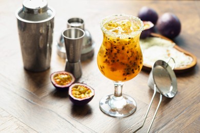 Photo of Tasty passion fruit drink in glass, fresh fruits and bartender's tools on wooden table, closeup