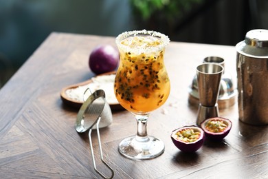 Photo of Tasty passion fruit drink in glass, fresh fruits and bartender's tools on wooden table