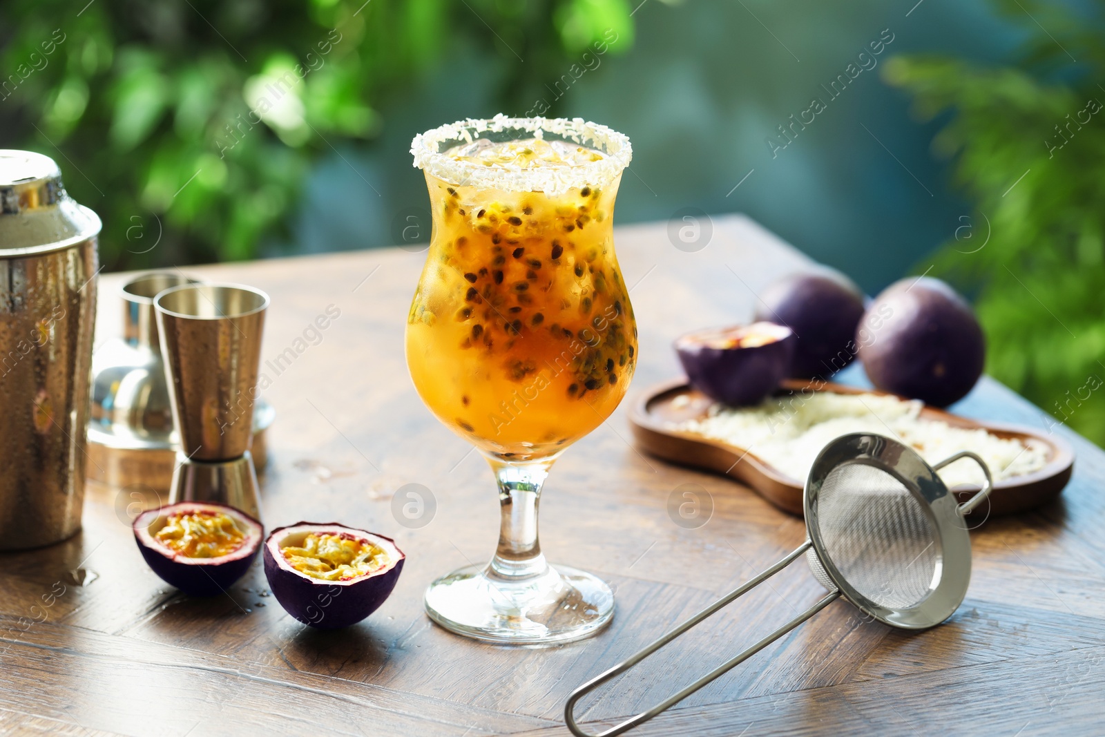 Photo of Tasty passion fruit drink in glass, fresh fruits and bartender's tools on wooden table