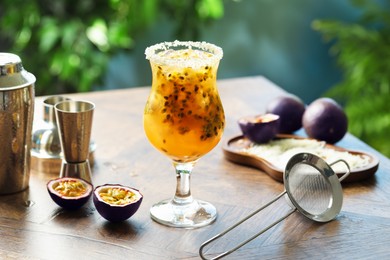 Photo of Tasty passion fruit drink in glass, fresh fruits and bartender's tools on wooden table