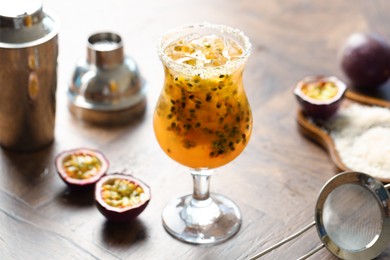 Photo of Tasty passion fruit drink in glass, fresh fruits, shaker and strainer on wooden table, closeup