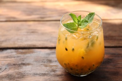 Photo of Tasty passion fruit drink with mint in glass on wooden table, closeup. Space for text