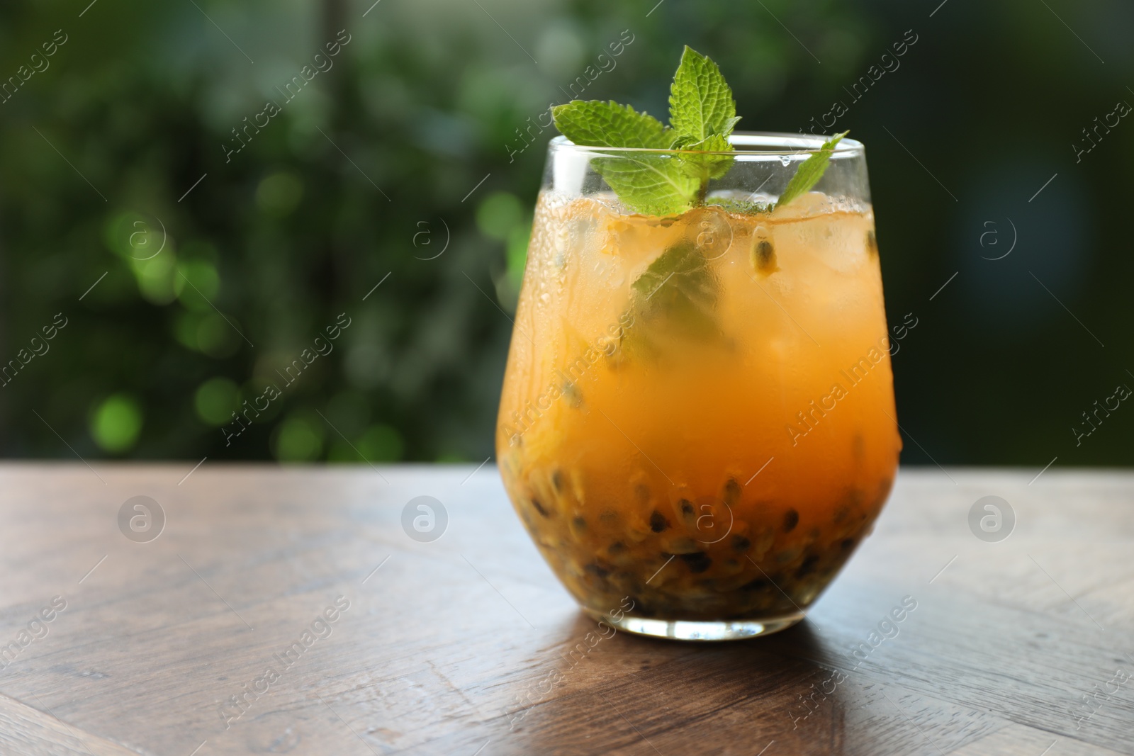 Tasty passion fruit drink with mint in glass on wooden table against blurred green, closeup. Space for text Photo of Tasty passion fruit drink with mint in glass on wooden table against blurred green, closeup. Space for text